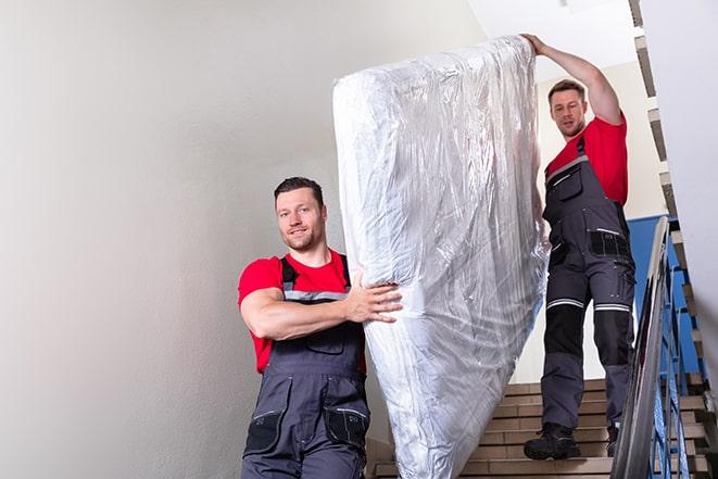 two people carrying a box spring out of a bedroom in Alton, TX